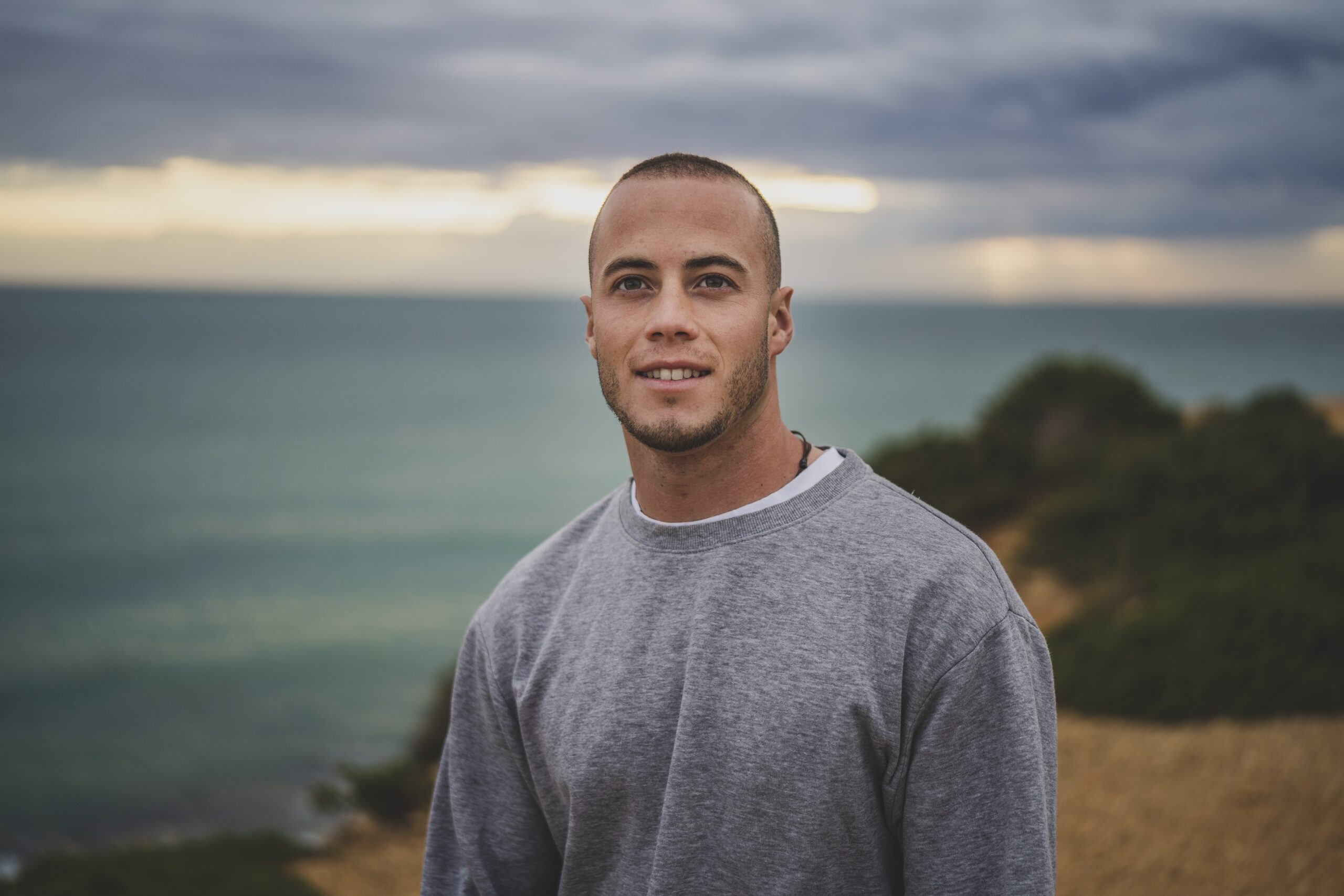 A young man smiling and standing on a cliff near the beautiful sea